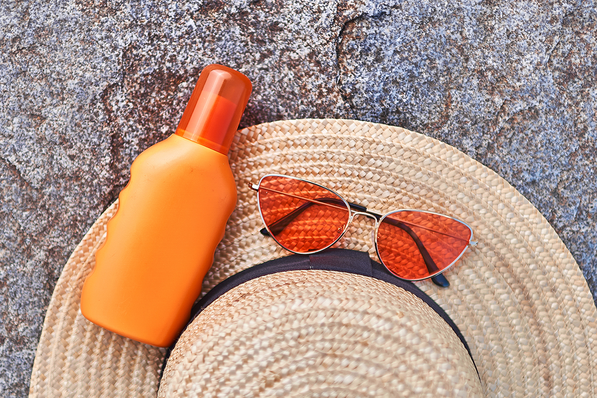 Straw hat, bright red glasses and orange bottle of sunscreen for sun protection